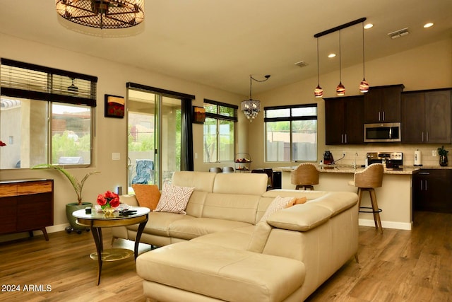 living room featuring a notable chandelier, vaulted ceiling, and light hardwood / wood-style flooring