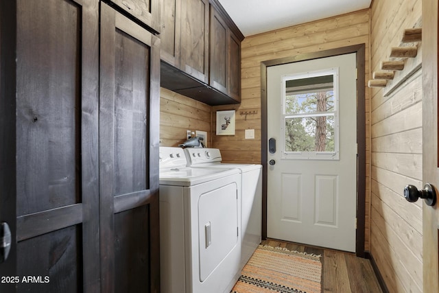 laundry area featuring cabinets, washing machine and clothes dryer, wooden walls, and light hardwood / wood-style floors