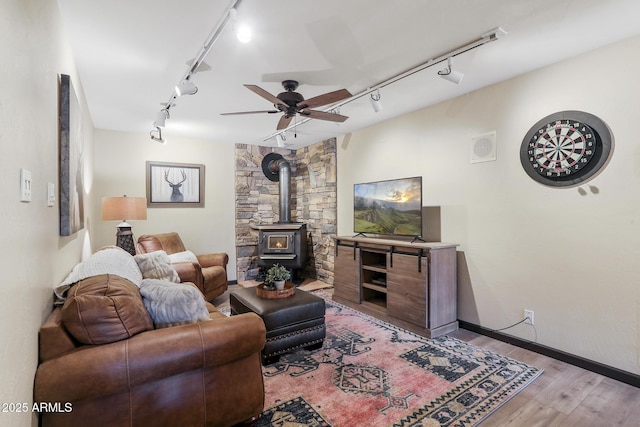 living room featuring a wood stove, track lighting, ceiling fan, and light hardwood / wood-style flooring