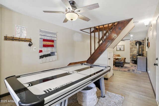 playroom with a wood stove, ceiling fan, and light wood-type flooring