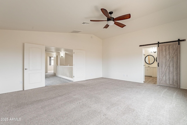 empty room with ceiling fan, a barn door, vaulted ceiling, and light colored carpet