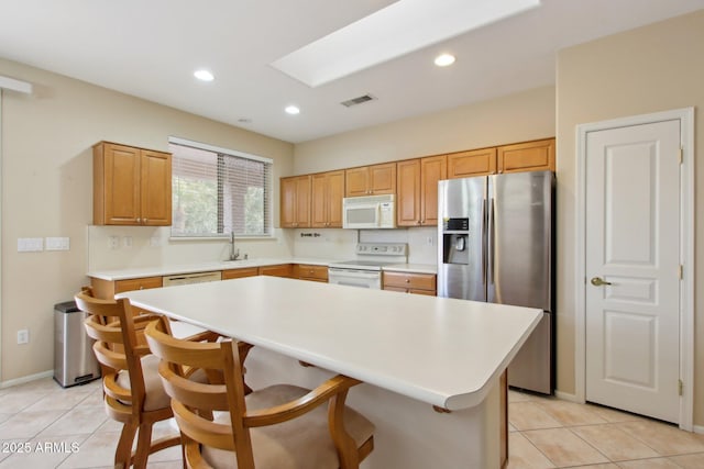 kitchen with a kitchen bar, a skylight, stainless steel appliances, a kitchen island, and light tile patterned flooring