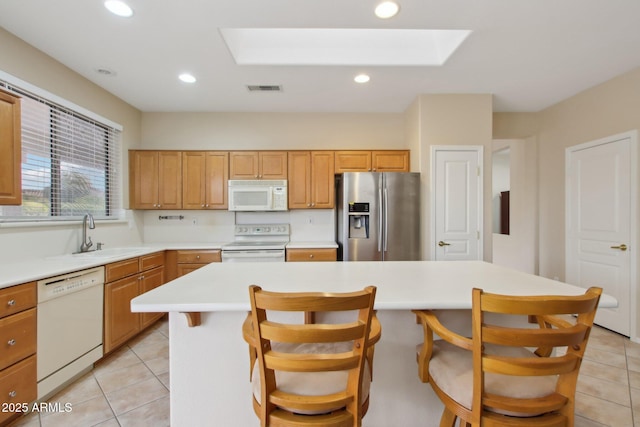 kitchen featuring a kitchen island, a skylight, a breakfast bar area, light tile patterned floors, and white appliances