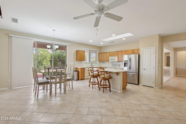 kitchen featuring light tile patterned flooring, a breakfast bar area, a kitchen island, pendant lighting, and white appliances