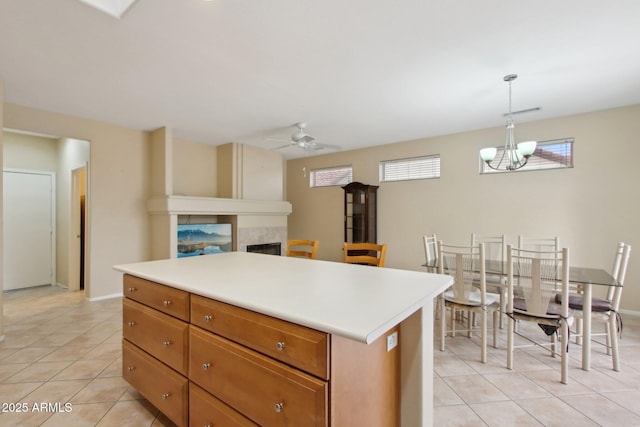 kitchen with a kitchen island, ceiling fan with notable chandelier, pendant lighting, a tiled fireplace, and light tile patterned floors