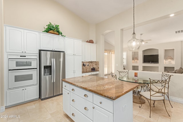 kitchen featuring a center island, stainless steel refrigerator with ice dispenser, double oven, light stone counters, and white cabinetry