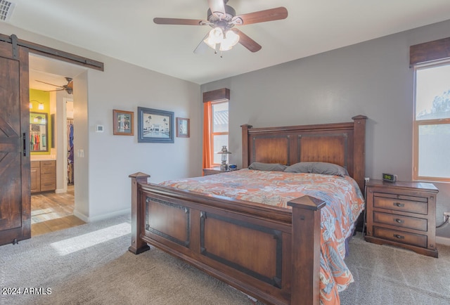 bedroom with a barn door, ensuite bath, light carpet, and ceiling fan