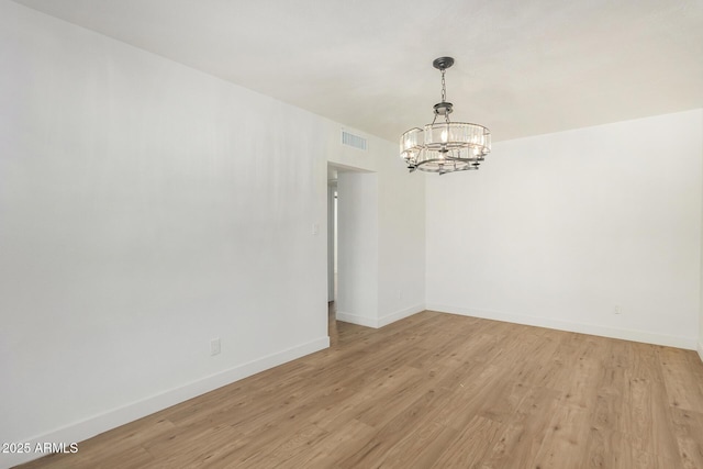 spare room with light hardwood / wood-style flooring and a notable chandelier