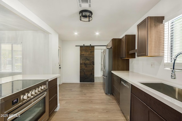 kitchen with a barn door, sink, stainless steel appliances, and light hardwood / wood-style floors