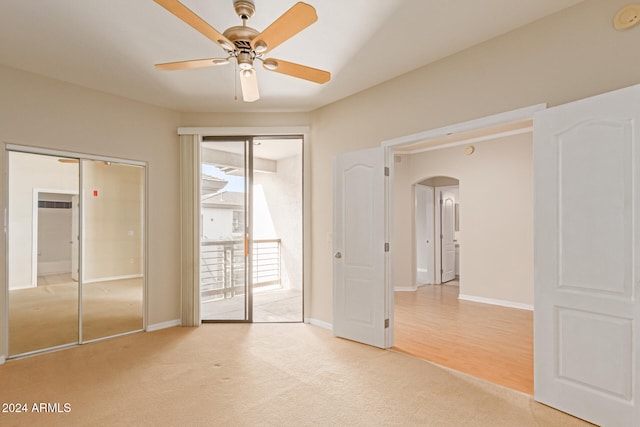 empty room with arched walkways, light colored carpet, ceiling fan, and baseboards