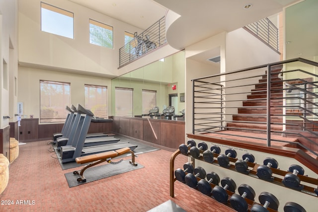 workout area with carpet flooring, a towering ceiling, and wooden walls