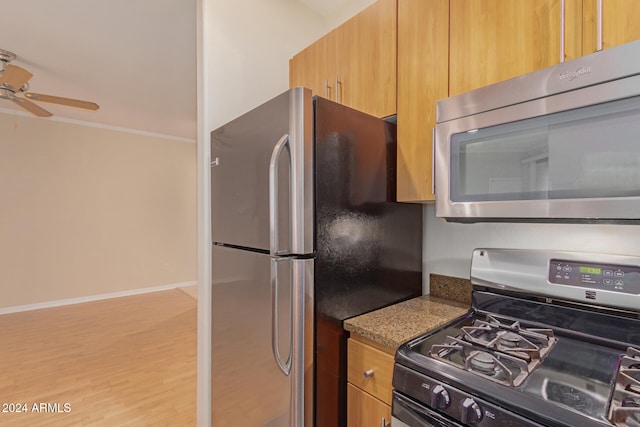 kitchen featuring ceiling fan, dark stone counters, light wood-type flooring, appliances with stainless steel finishes, and ornamental molding