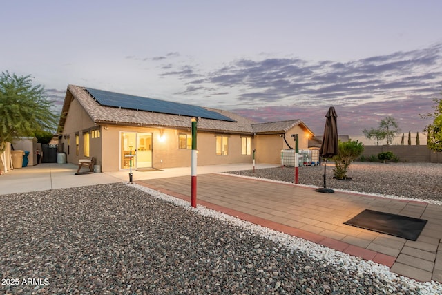 136 N 236th Ave, Buckeye, AZ 85396 - back of house at dusk featuring solar panels, stucco siding, fence, and a patio area