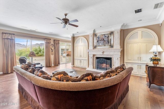 living room with ceiling fan, a high end fireplace, ornamental molding, and wood-type flooring