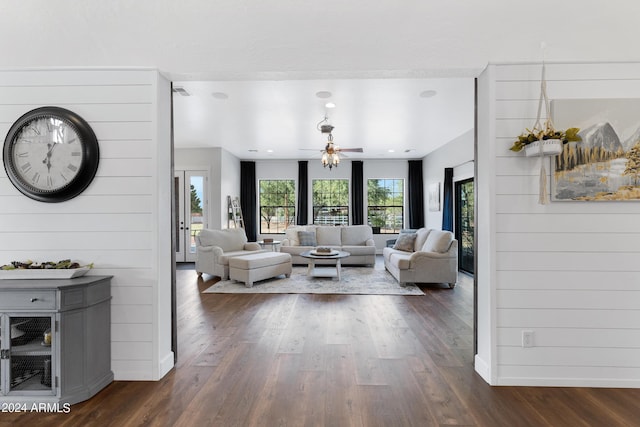 living room with wood walls, dark wood-type flooring, and ceiling fan