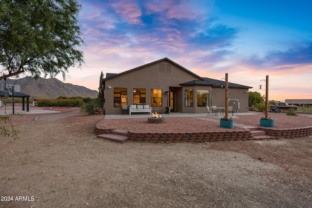 back house at dusk with a mountain view, a patio, and a fire pit