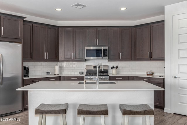 kitchen with sink, a kitchen island with sink, stainless steel appliances, a kitchen breakfast bar, and decorative backsplash