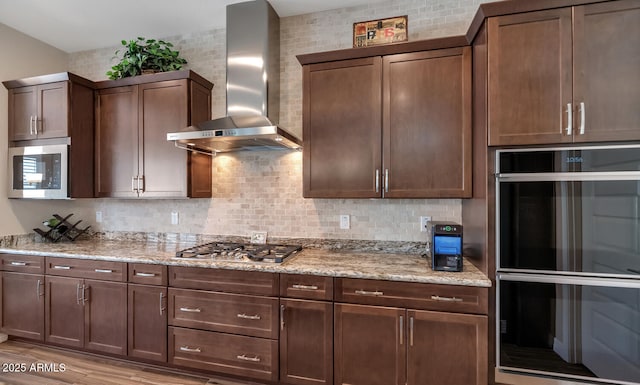 kitchen with appliances with stainless steel finishes, decorative backsplash, light stone counters, and wall chimney exhaust hood