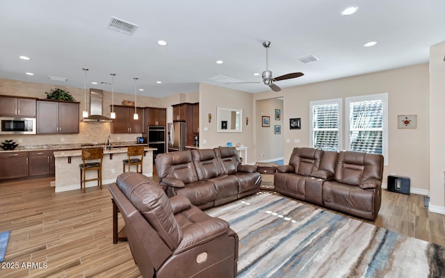 living room with ceiling fan, sink, and light wood-type flooring