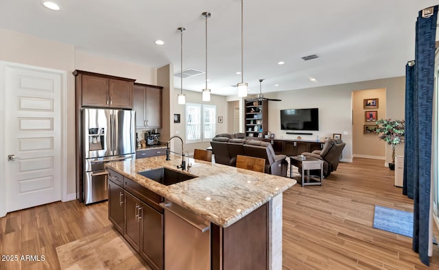 kitchen featuring appliances with stainless steel finishes, an island with sink, sink, dark brown cabinetry, and light hardwood / wood-style floors