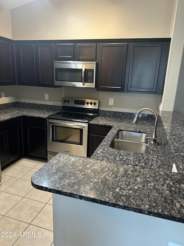 kitchen with light tile patterned floors, stainless steel appliances, dark stone counters, and sink