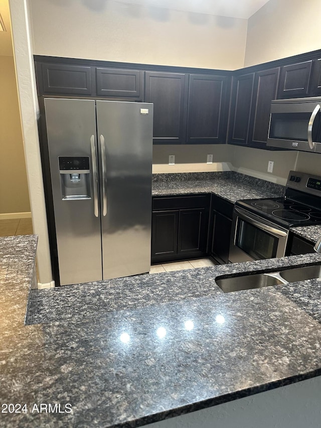 kitchen featuring sink, light tile patterned floors, stainless steel appliances, and dark stone counters