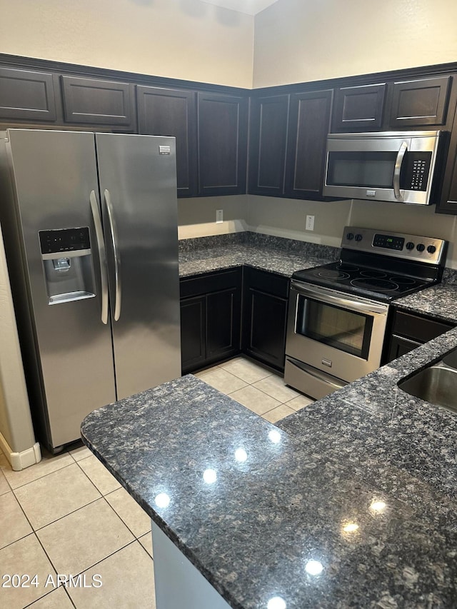 kitchen with appliances with stainless steel finishes, sink, light tile patterned floors, and dark stone countertops