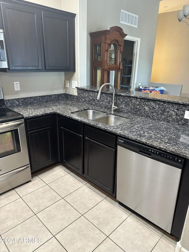 kitchen with sink, dark stone countertops, light tile patterned floors, a notable chandelier, and stainless steel appliances