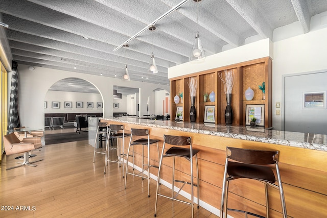 kitchen with a breakfast bar, a textured ceiling, stone countertops, track lighting, and light hardwood / wood-style flooring