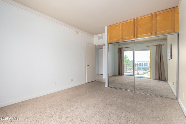 unfurnished bedroom featuring light carpet, ornamental molding, and a closet