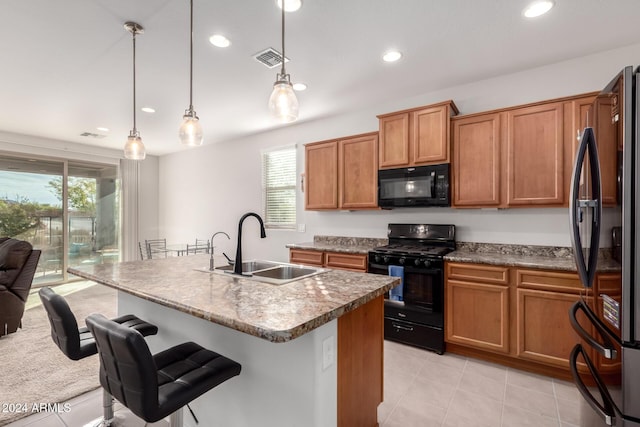 kitchen with brown cabinets, decorative light fixtures, a center island with sink, a sink, and black appliances