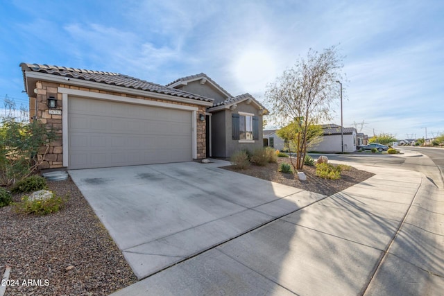 single story home featuring driveway, stone siding, an attached garage, and a tiled roof