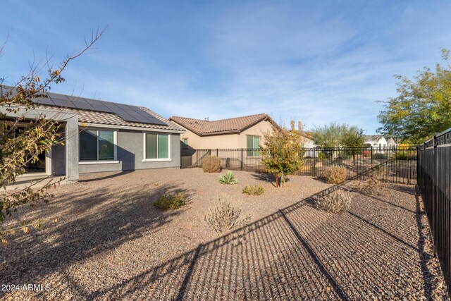 rear view of house with a tiled roof, stucco siding, a fenced backyard, and roof mounted solar panels