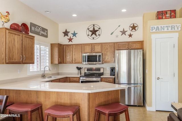 kitchen with sink, light tile patterned floors, a breakfast bar area, stainless steel appliances, and kitchen peninsula