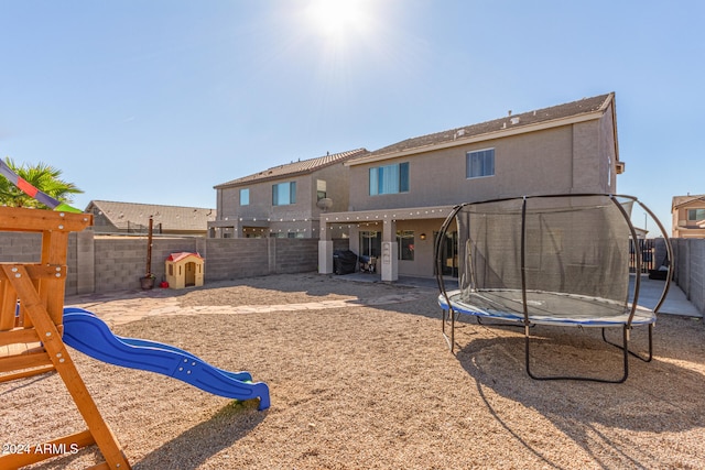 back of property featuring a playground and a trampoline