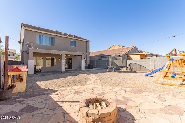 back of property with a fire pit, a trampoline, central AC, a patio area, and a playground