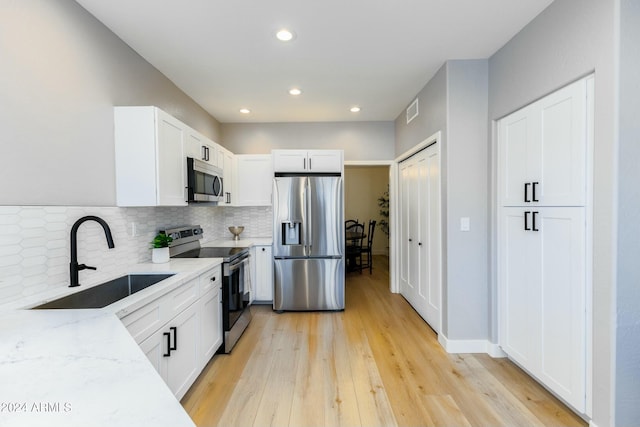 kitchen with white cabinetry, sink, stainless steel appliances, and light hardwood / wood-style flooring