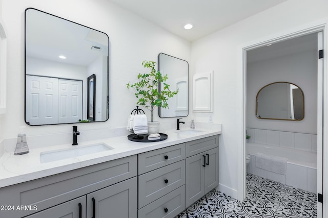 bathroom with tile patterned floors, vanity, a relaxing tiled tub, and toilet