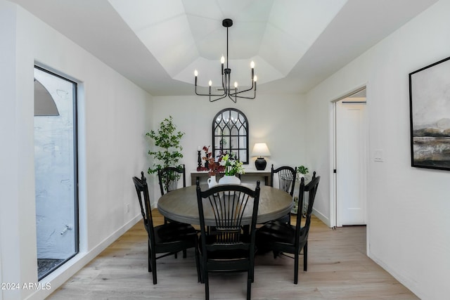 dining room featuring a notable chandelier, a raised ceiling, and light hardwood / wood-style flooring