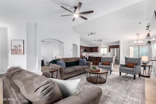 living room featuring lofted ceiling, ceiling fan with notable chandelier, light hardwood / wood-style flooring, and rail lighting