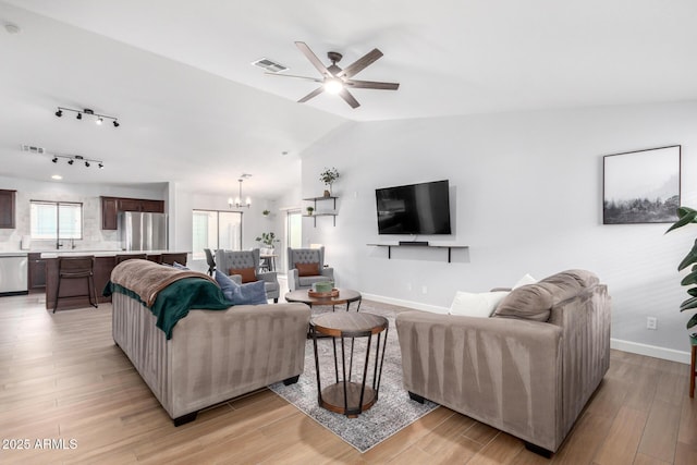 living room featuring vaulted ceiling, ceiling fan with notable chandelier, and light hardwood / wood-style floors