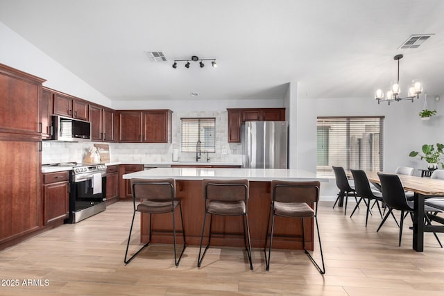 kitchen featuring sink, appliances with stainless steel finishes, hanging light fixtures, a center island, and a notable chandelier