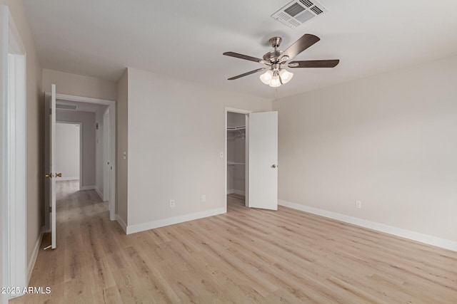 unfurnished bedroom featuring a walk in closet, a closet, visible vents, light wood-style flooring, and baseboards