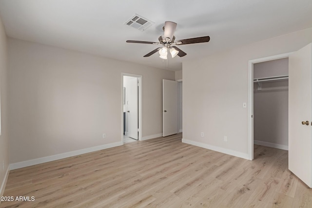 unfurnished bedroom featuring a walk in closet, light wood finished floors, a closet, visible vents, and baseboards