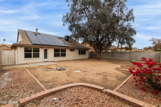 back of property with central AC unit, a fenced backyard, solar panels, roof with shingles, and a patio area