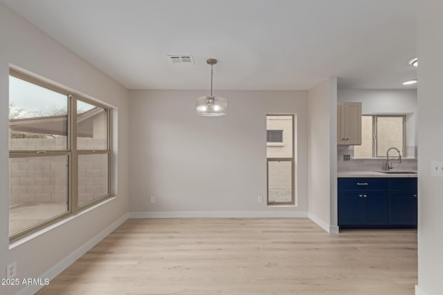 unfurnished dining area featuring baseboards, light wood-style flooring, visible vents, and a sink