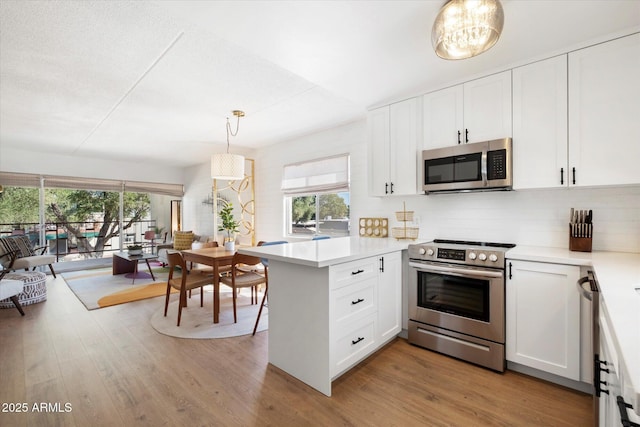 kitchen with stainless steel appliances, light countertops, white cabinetry, light wood-type flooring, and a peninsula