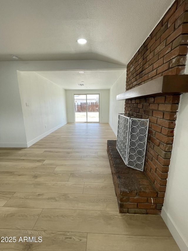 unfurnished living room featuring light wood-style floors, lofted ceiling, a textured ceiling, and baseboards