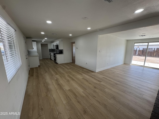 unfurnished living room with recessed lighting, light wood-style flooring, and baseboards