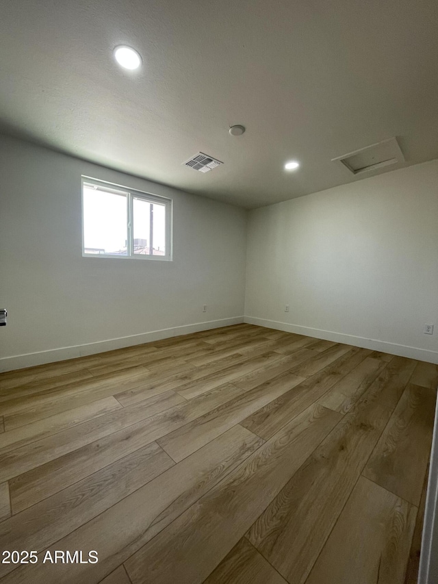 unfurnished room featuring baseboards, light wood-style flooring, visible vents, and attic access